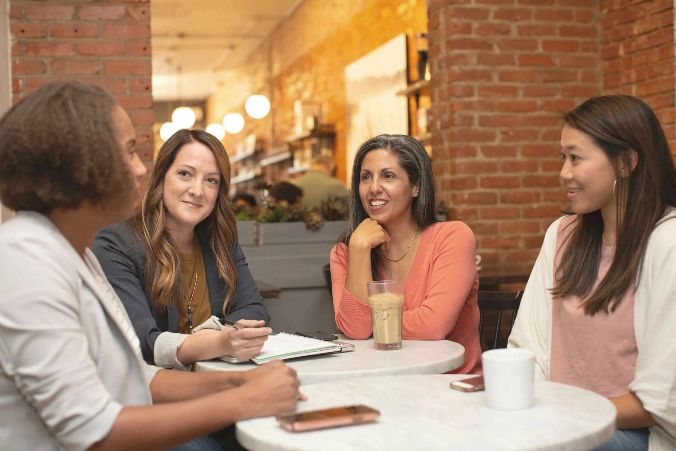 Quatre femmes échangent autour d’une table de café, un carnet ouvert.